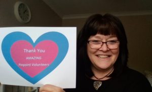 A photo of Linda, our Volunteer manager. She has a huge smile of gratitude on her face and is holding up a sign that says "Thank you amazing Pinpoint Volunteers" in a pink and blue heart. 