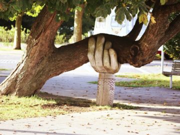 sculpture of a hand coming out of the ground and supporting the branch of a tree